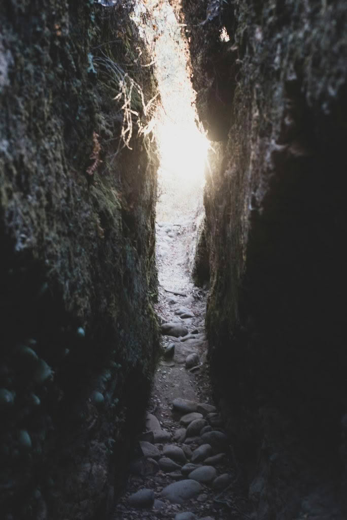 Narrow rocky passage between two stone walls opening into sunlight, symbolizing the narrow gate and hard road Jesus describes in Matthew 7:13-14